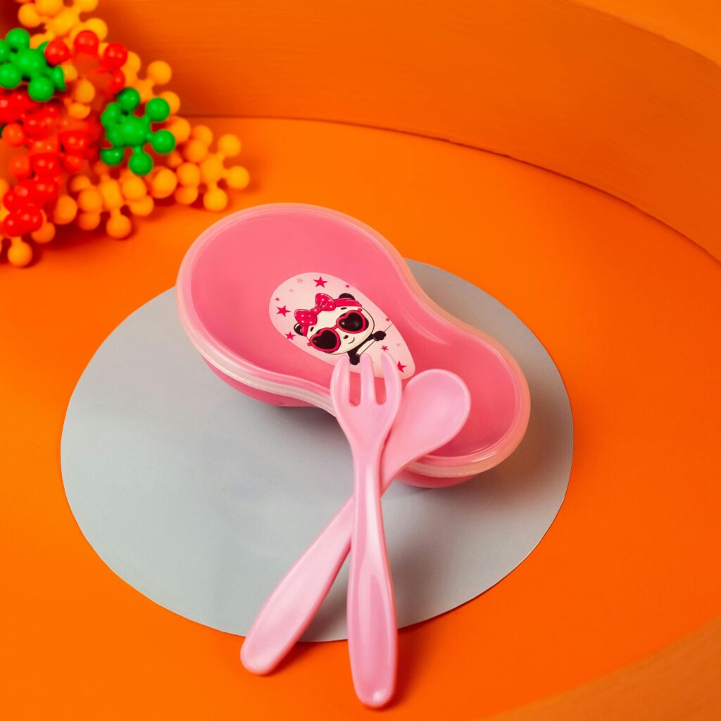 Bright pink kids tableware set with fork and spoon on an orange background.